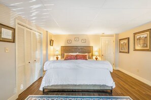 Ein Schlafzimmer mit einem hölzernen Bett, zwei Nachttischlampen, einem Holz-Kopfende, einer Tür und einem Fenster mit Jalousien.