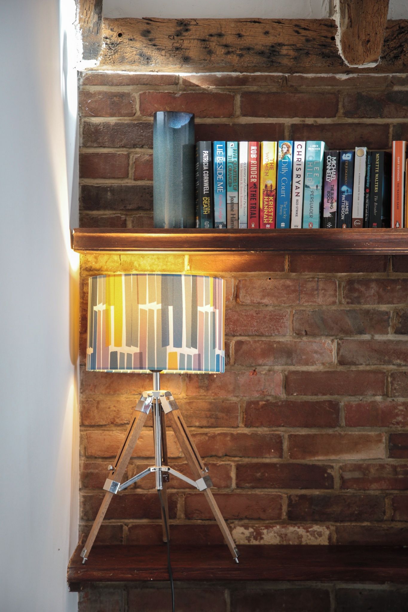 A bookshelf against a brick wall with a tripod lamp in front.