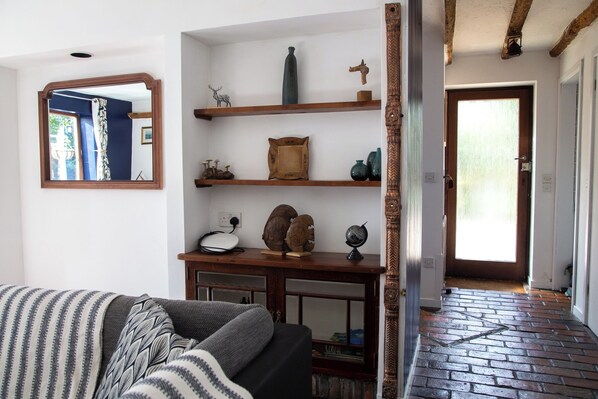 Una sala de estar con un sofá, estanterías de madera con adornos, un espejo y una puerta que da a otra habitación.