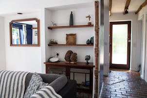 A living room with a sofa, wooden shelves with decorative items, a mirror, and a door leading to another room.