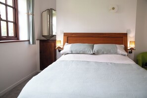 A neatly made bed with a wooden headboard, two bedside lamps, and a mirror on the wall. - Sleeps 5 With in Picturesque Chiddingly (Lewes)