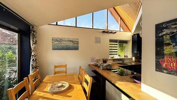 A modern kitchen with a wooden table and chairs, a window with a view of the outside, and a poster on the wall.
