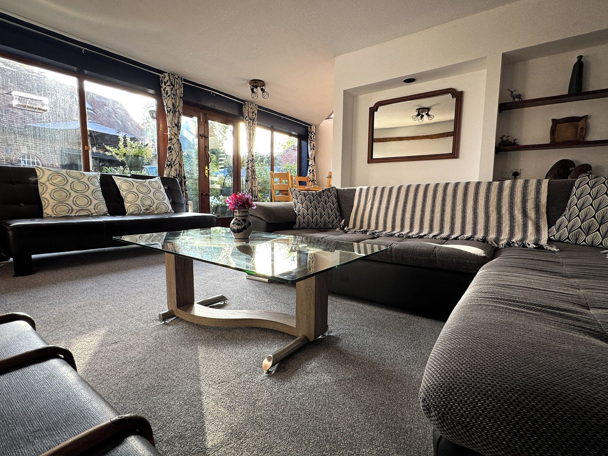 Ein modernes Wohnzimmer mit einem Glastisch, zwei Sofas und einem großen Fenster mit Blick ins Freie.