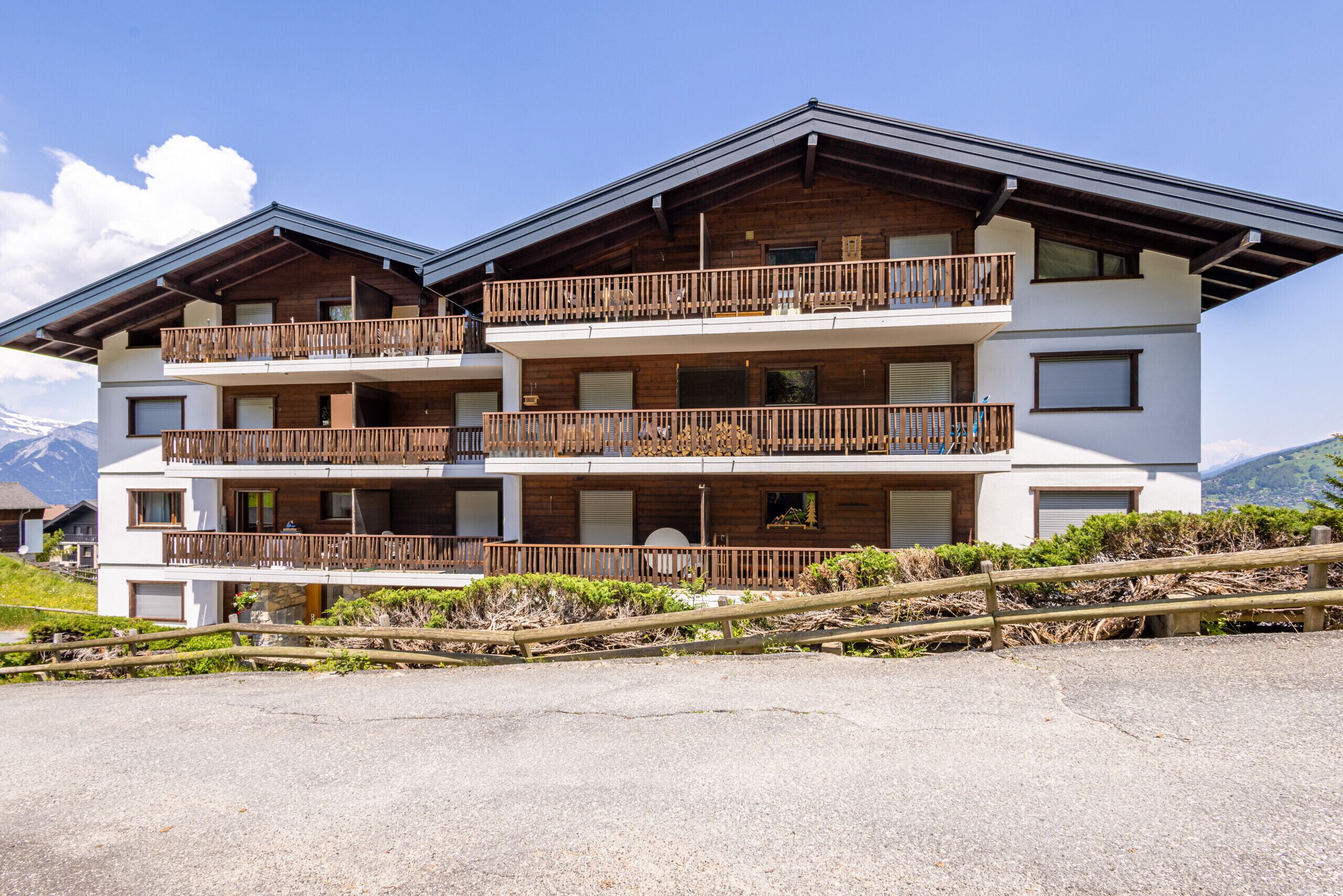 A multi-story building with balconies, a wooden facade, and a mountainous backdrop.