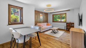 Uma sala de estar moderna com área de jantar, piso de madeira, sofá, mesa de centro e televisão na parede.