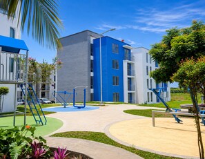 A modern apartment building with a blue and white facade, outdoor exercise equipment, and a well-maintained garden area. - Modern apartment in Quindío with a pool (Quindío)