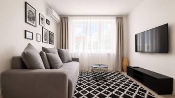 Een moderne woonkamer met een bank, een rond bijzettafeltje, een zwart-wit vloerkleed, een flatscreen televisie en ingelijste foto's aan de muur.