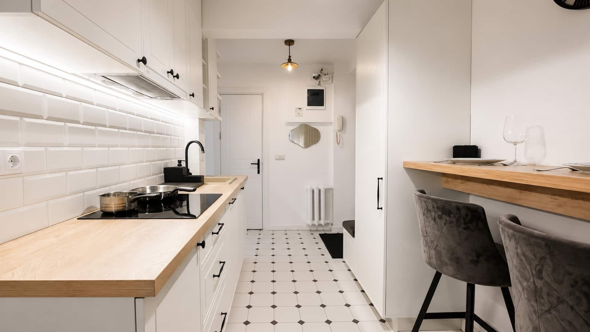 A modern kitchen with white cabinets, a wooden countertop, a black faucet, and a tiled floor.