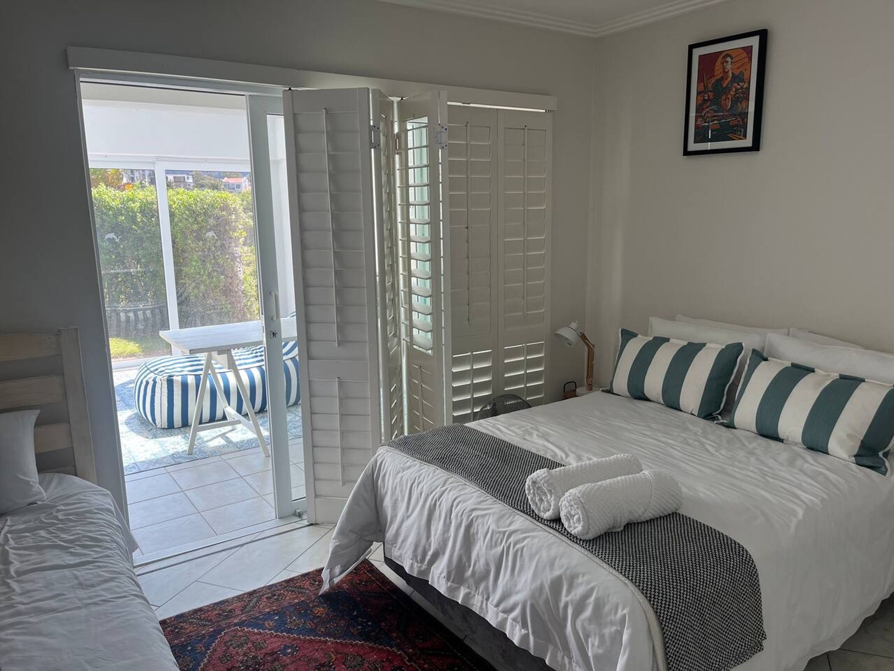 A bedroom with a bed, a desk, and a chair. There is a sliding door leading to an outdoor area with a table and chairs.