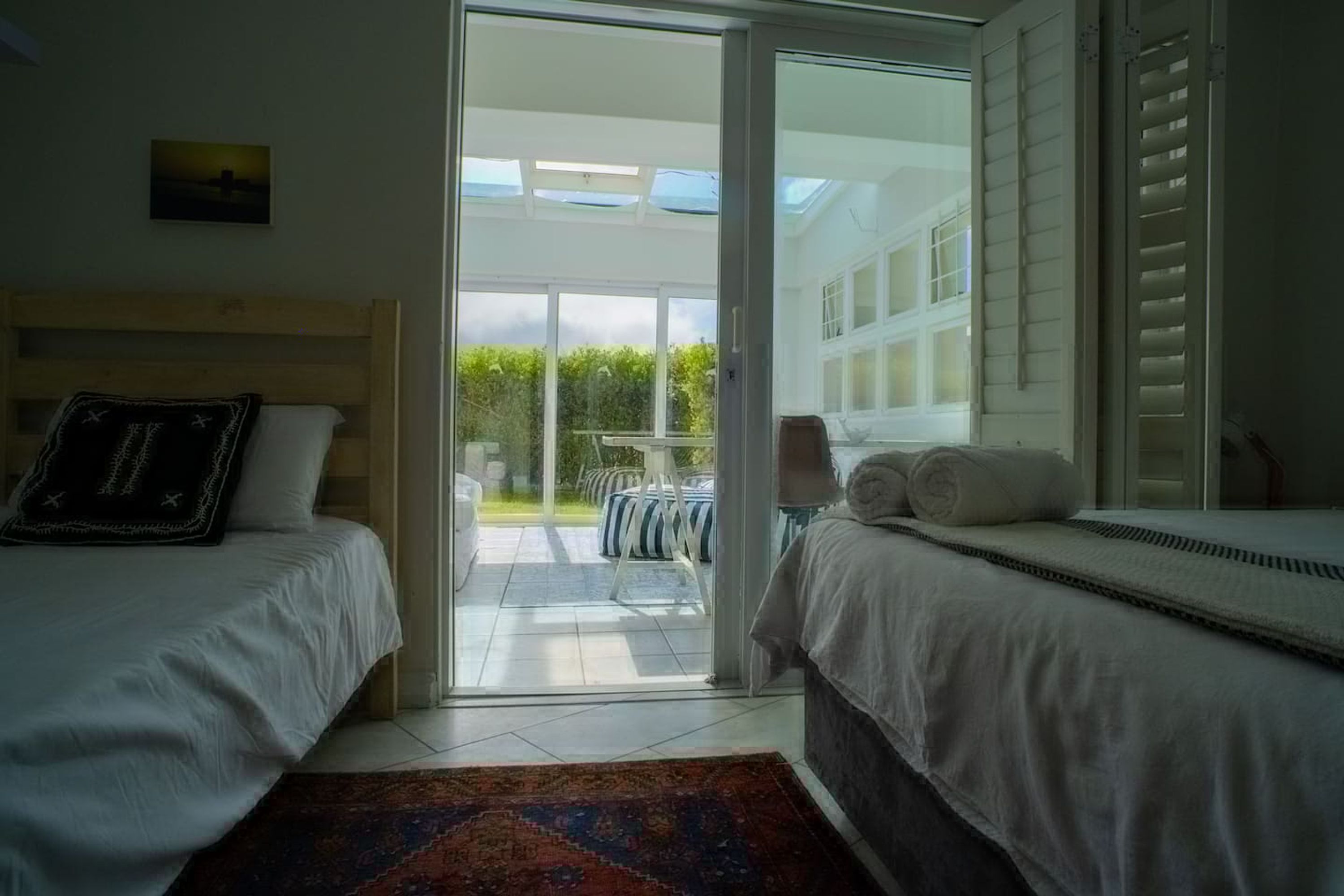 Un dormitorio con dos camas, un amplio ventanal corredero que da a un patio y vistas a zonas verdes.