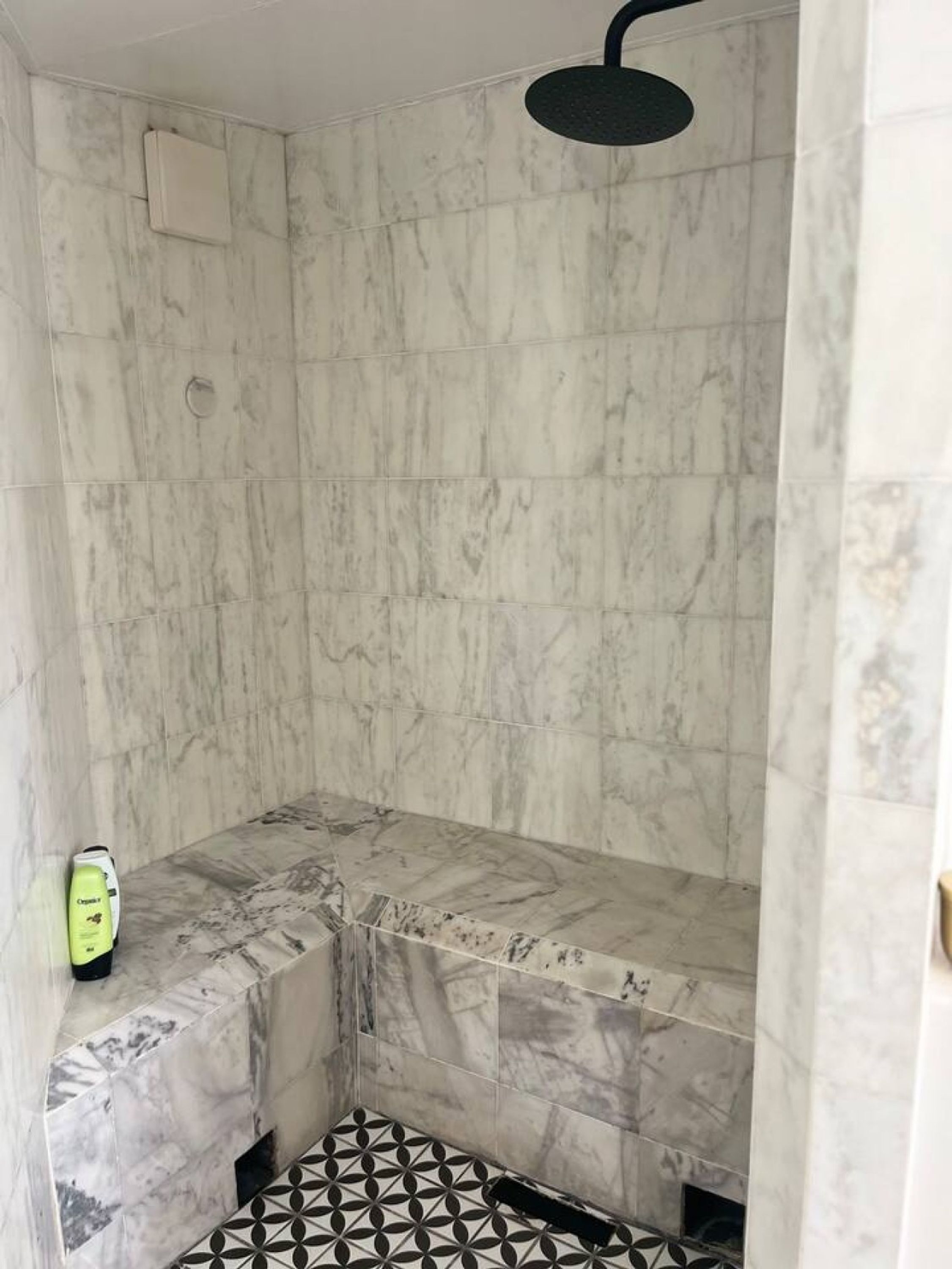 Un baño con ducha, paredes de mármol y suelo estampado.