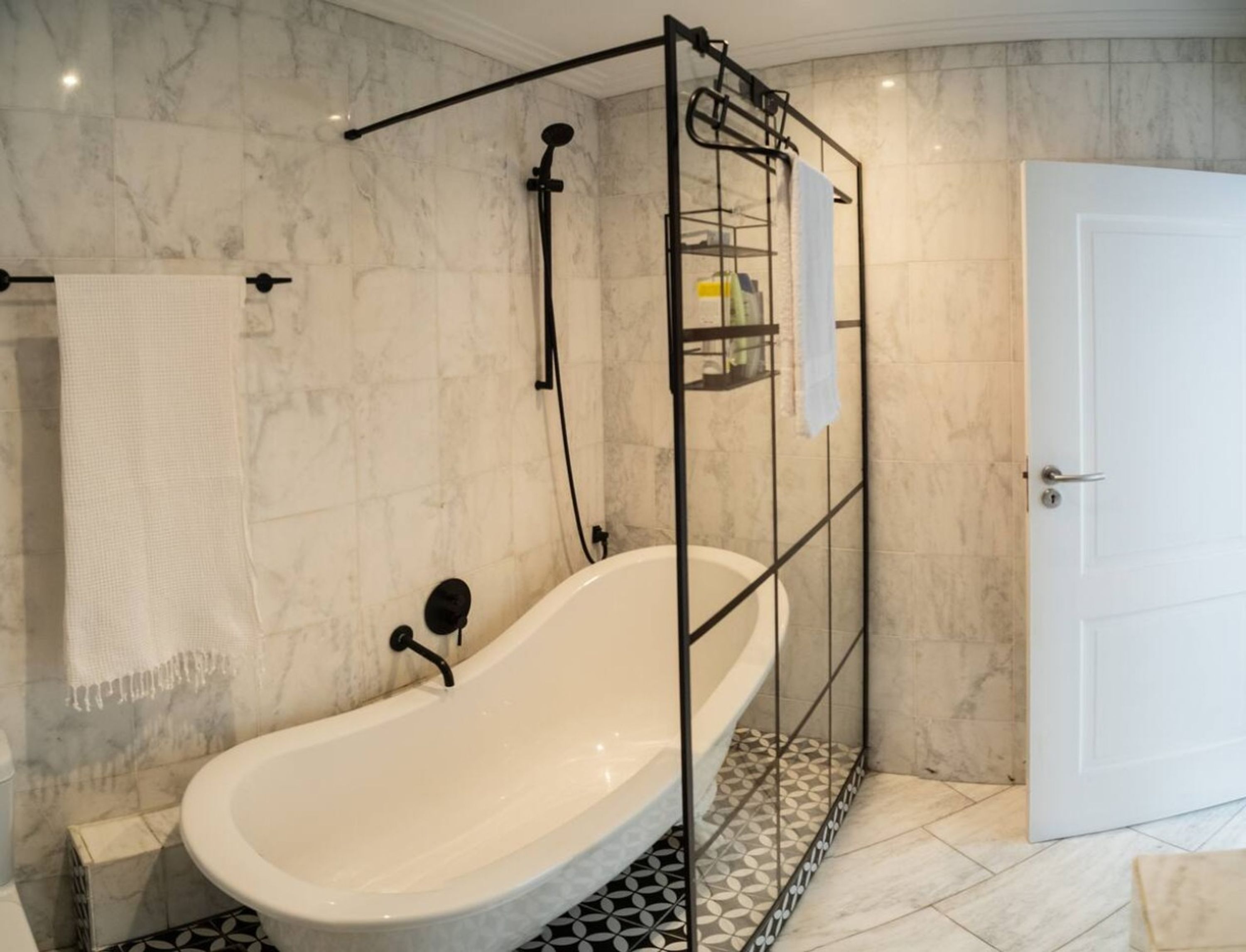 A bathroom with a freestanding bathtub, a towel rack, a shower head, and a door.