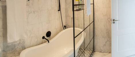 A bathroom with a freestanding bathtub, a towel rack, a shower head, and a door.