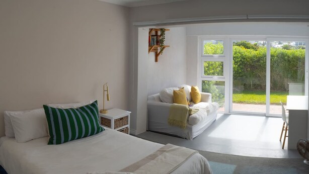 A bedroom with a large bed, a smaller sofa, a desk, and a sliding glass door leading to a balcony. - Beachfront Designer Villa in Secure Estate (Cape Town)