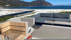 A rooftop terrace with a view of a beach and mountains, a grill area, and a seating area. - Beachfront Designer Villa in Secure Estate (Cape Town)