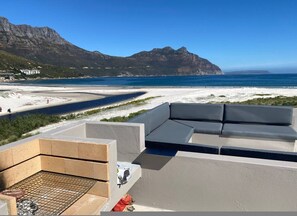 Eine Dachterrasse mit Blick auf Strand und Berge, ein Grillbereich und eine Sitzgelegenheit.