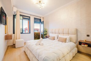 A modern bedroom with a large bed, a bedside table, a TV, and a view of the outside. - Luxury Apt in Heart Gueliz  Panoramic City Views MARRAKECH (Marrakech)
