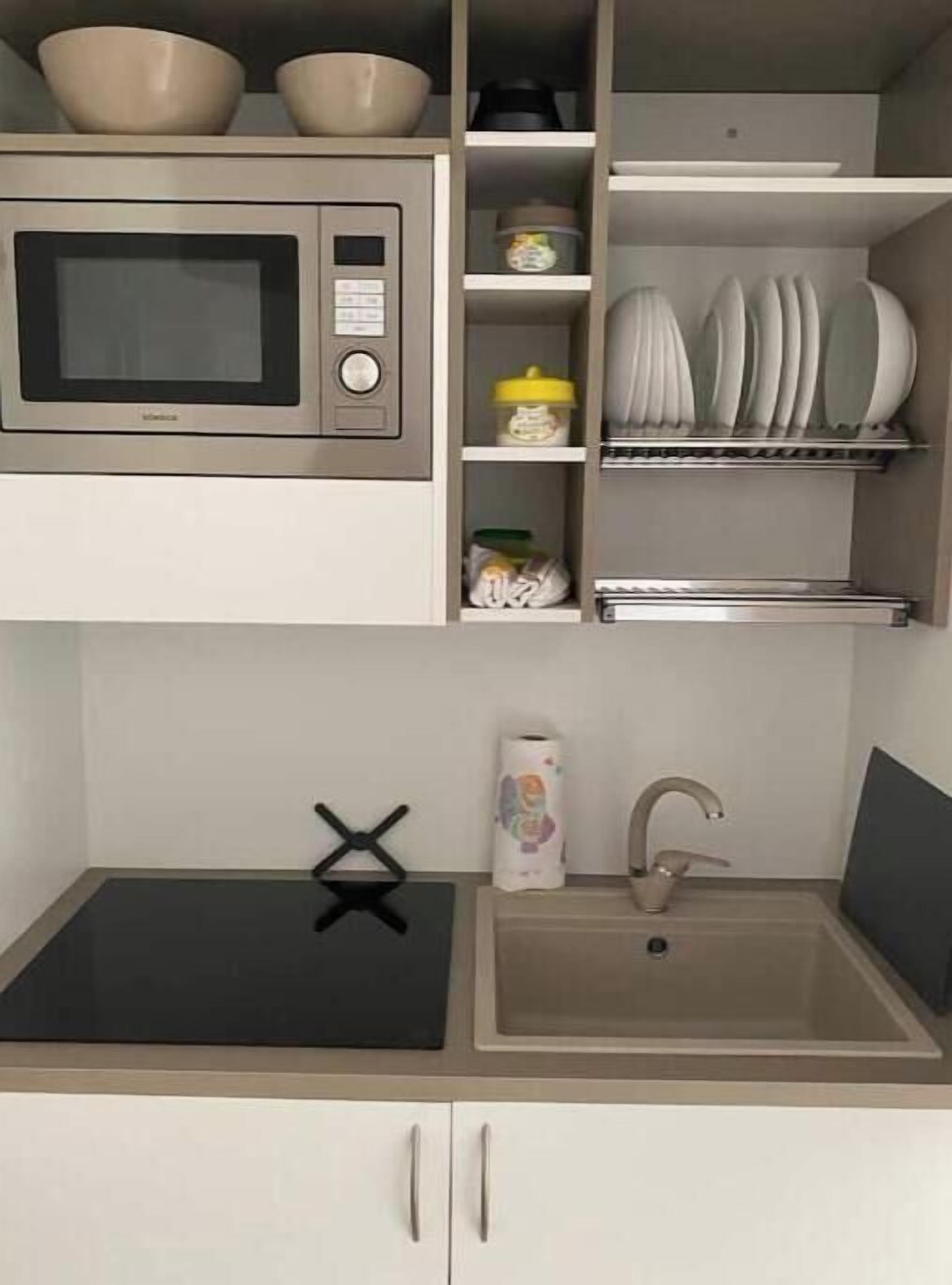 A kitchen with a microwave, sink, and storage shelves.