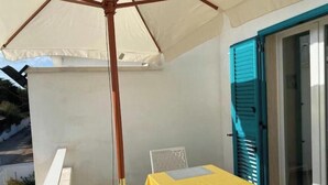 Un balcon avec une table et une chaise, un parasol blanc et une porte bleue.