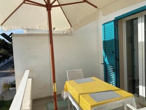A balcony with a table and chair, a white umbrella, and a blue door. - Amida App.to, Cielo, 1st Floor (Campomarino di Maruggio (TA))