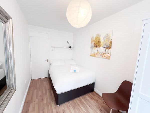 Ein Schlafzimmer mit einem Bett, einem Sessel, einem Gemälde, einer Tür und einer Deckenleuchte.