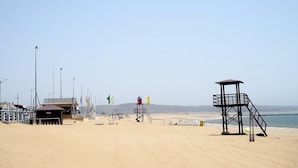 A beach with lifeguard towers, a small building, and a fence.