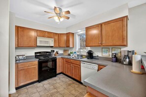 A kitchen with wooden cabinets, a stove, a microwave, a dishwasher, and a ceiling fan. - Spacious Woodland Cabin with Fire Pit & Creek Near Berkeley Springs, West Virginia (Berkeley Springs)