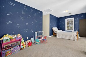 Una stanza giochi per bambini con un muro decorato con stelle, un letto e una finestra vista alberi.