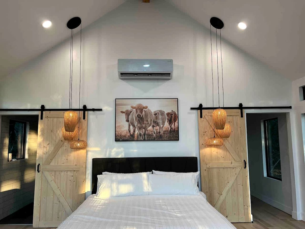 A bedroom with a large bed, wooden barn doors, an air conditioning unit, and a painting of cows.