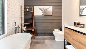 Ein modernes Badezimmer mit Badewanne, Toilette und einem Holzbodenregal.