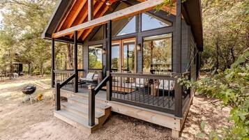 Une cabane avec une véranda, un espace salon extérieur et un barbecue.