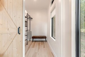 A hallway with a wooden door, a bench, a radiator, and a window with a view of trees.