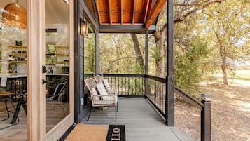 A wooden deck with a glass door leading to a kitchen area, a bench with cushions, and a 'HELLO' mat.