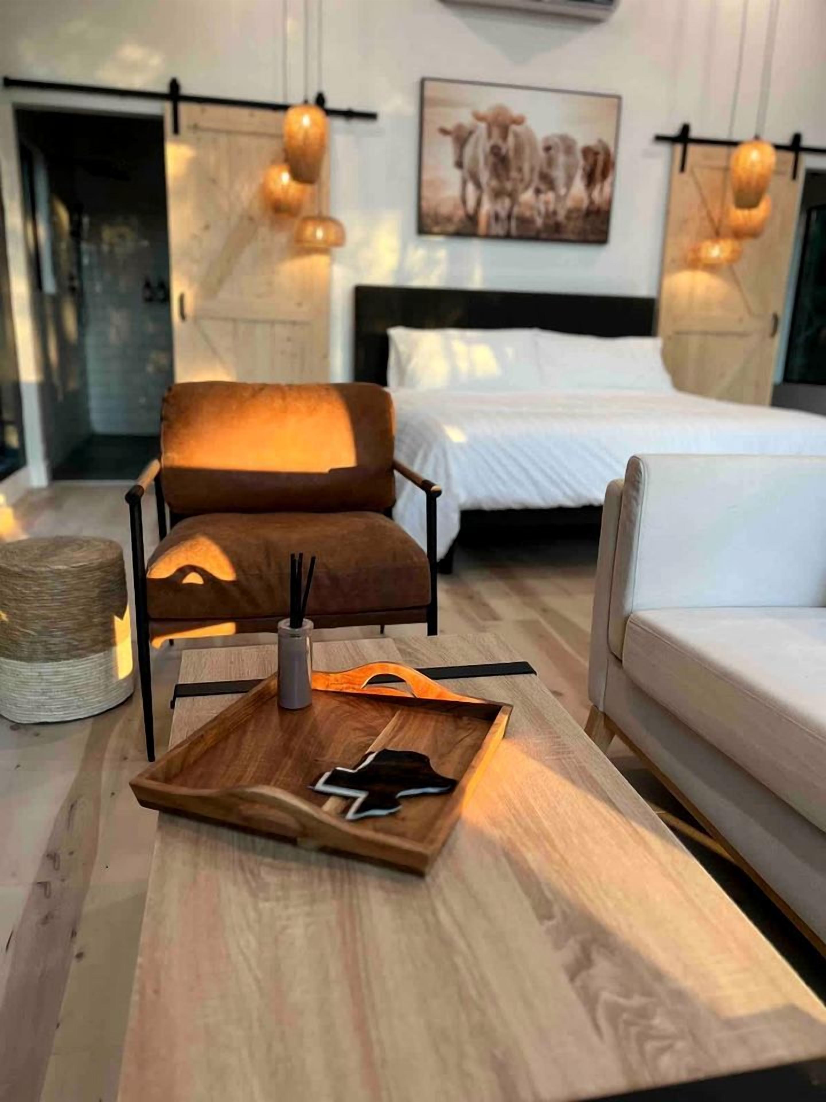A modern bedroom with a bed, a brown chair, a wooden side table, and a wall-mounted light fixture.