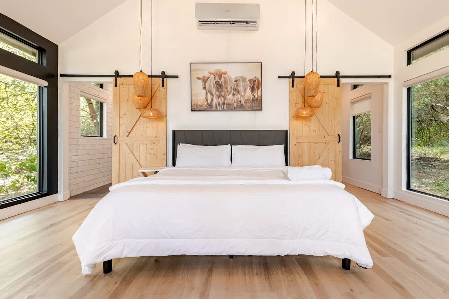 A modern bedroom with a large bed, wooden slats, a painting of cows, and large windows.