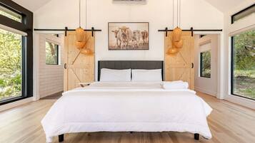 A modern bedroom with a large bed, wooden slats, a painting of cows, and large windows.