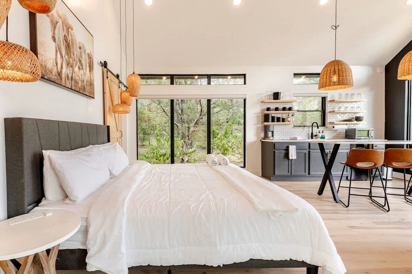 A modern bedroom with a large bed, a small table, and a view of the outdoors.