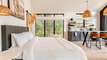 A modern bedroom with a large bed, a small table, and a view of the outdoors.