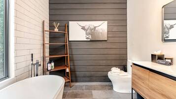 A modern bathroom with a bathtub, toilet, and wooden shelving unit.