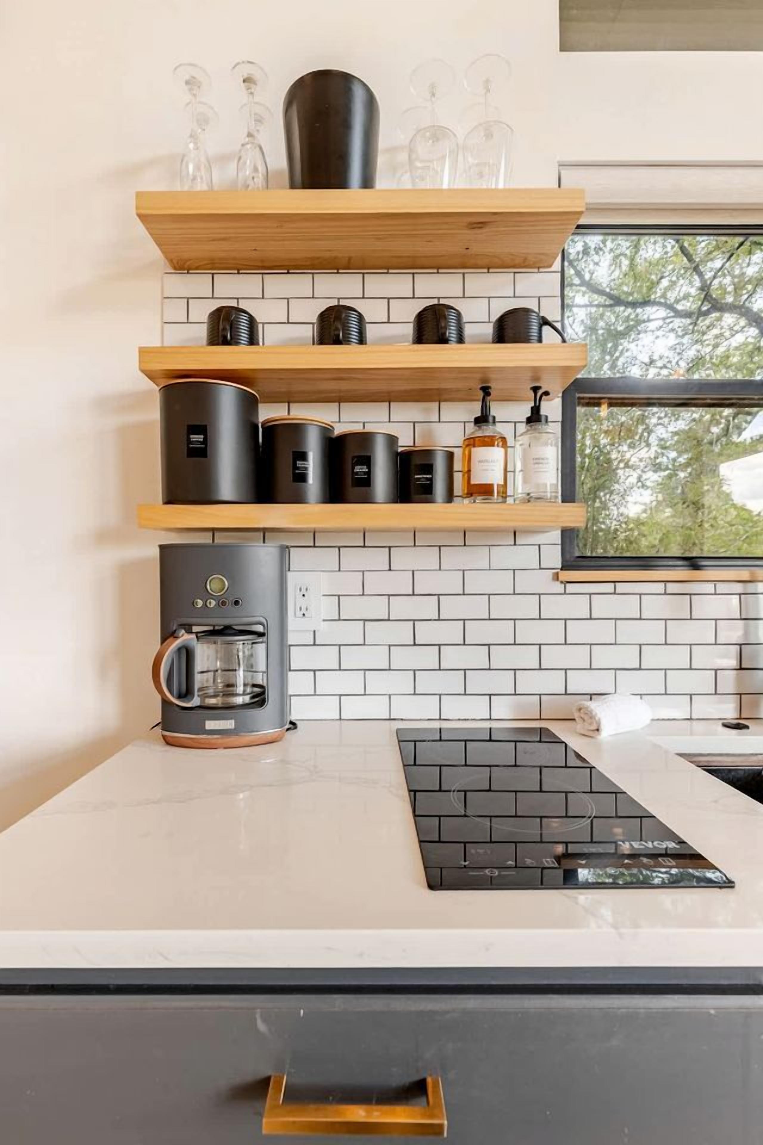 A modern kitchen with a coffee machine, shelves with glassware, and a window with a view.