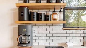 A modern kitchen with a coffee machine, shelves with glassware, and a window with a view.