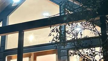 A modern house with a large glass window and a visible moon through the tree branches.