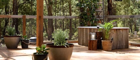 Une terrasse en bois agrémentée de plantes en pot, d’une cafetière en métal et d’un tonneau en bois.