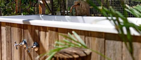 Una terraza de madera con una bañera blanca, un grifo de metal y un taburete de madera.