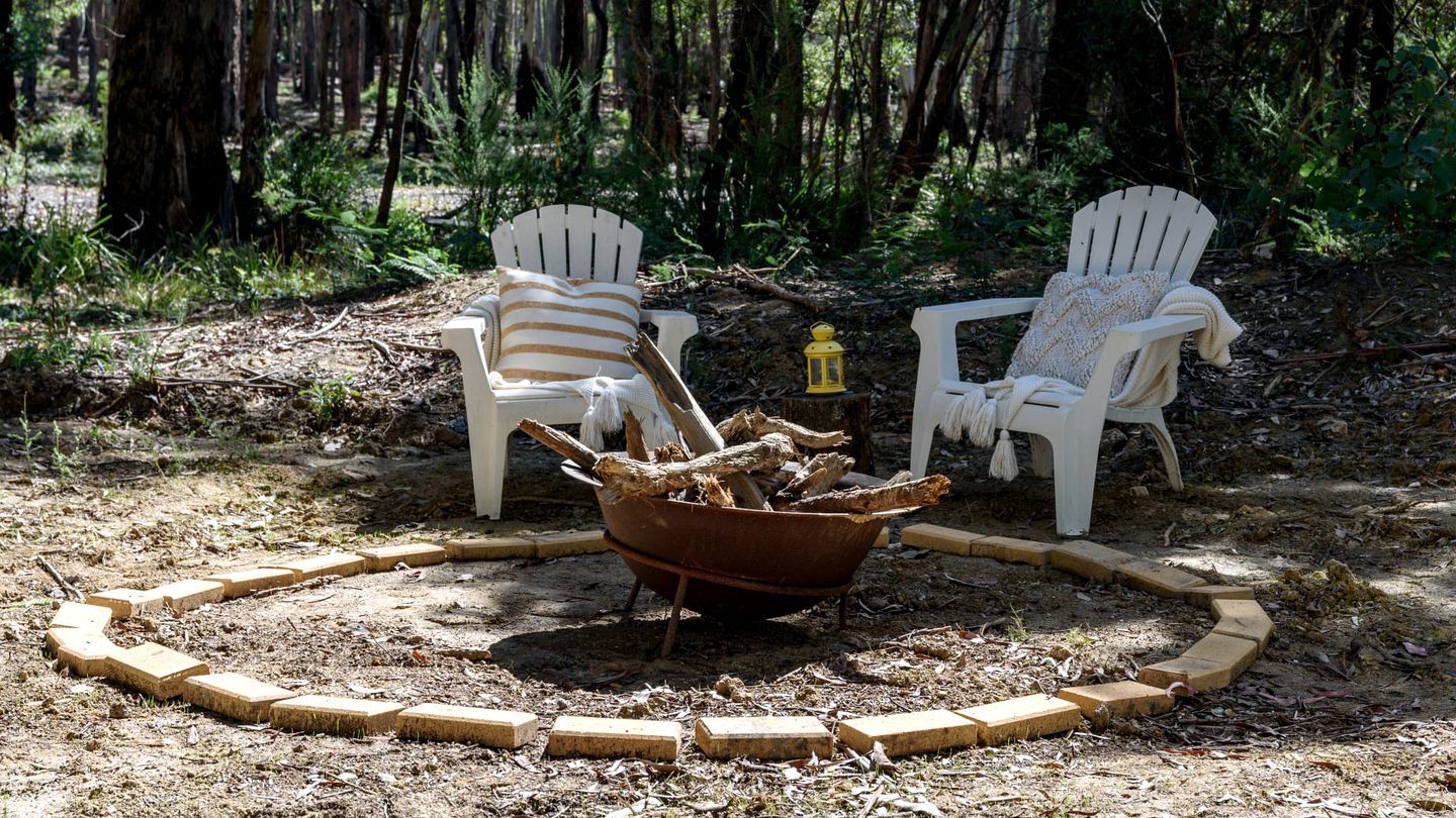 Two white Adirondack chairs with striped cushions, a fire pit with logs, and a lantern.