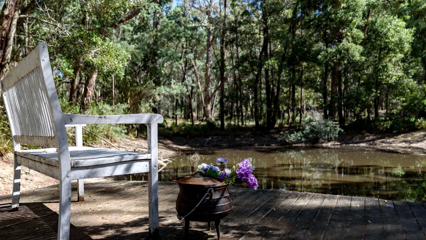 A bench, a rustic pot, and a pond in a wooded area.