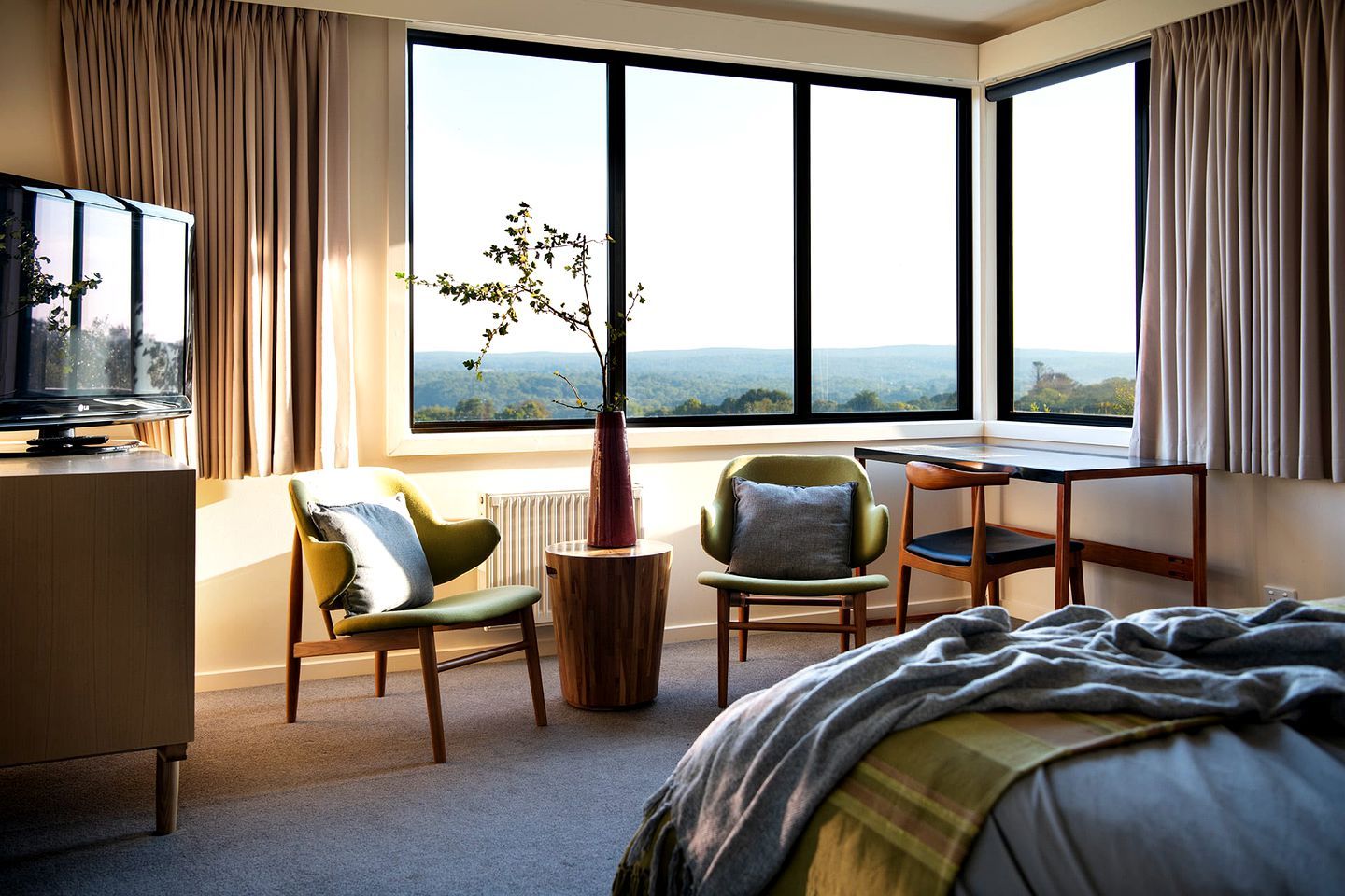 A hotel room with a bed, a desk, two chairs, a television, and a large window with a view.