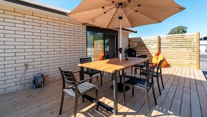 Une terrasse avec une table en bois, des chaises et un grand parasol.