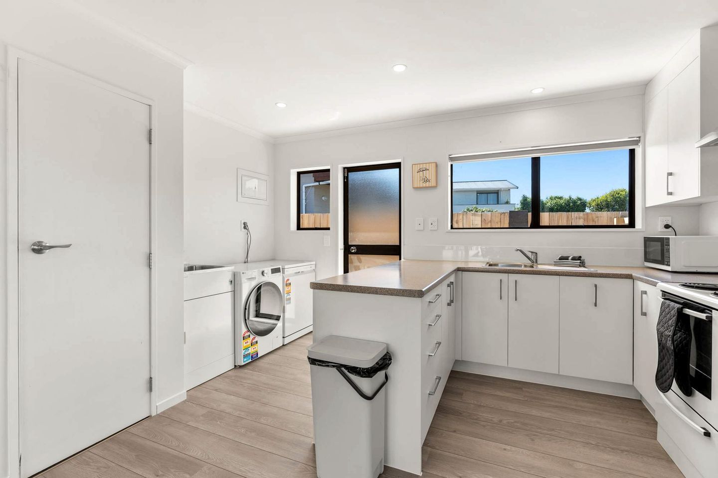 A modern kitchen with a built-in washer, a trash bin, and a view of the outside.