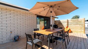 Eine Terrasse mit einem Holztisch, Stühlen und einem großen Sonnenschirm.